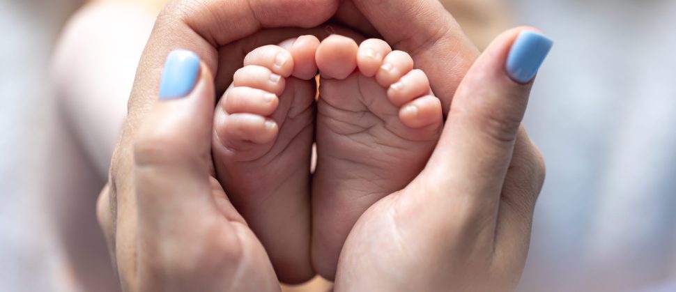 Page Ville de Castres – Naissance Mom holds the legs of a newborn baby in her hands, close-up, soft focus, concept of motherhood and care.